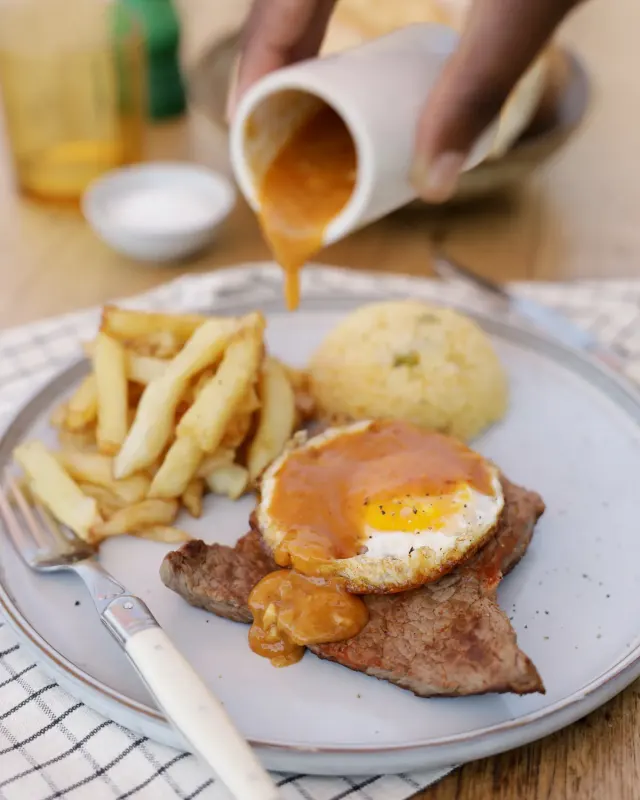 Portuguese steak and egg with sauce being poured - Parreirinha Rapido Illovo